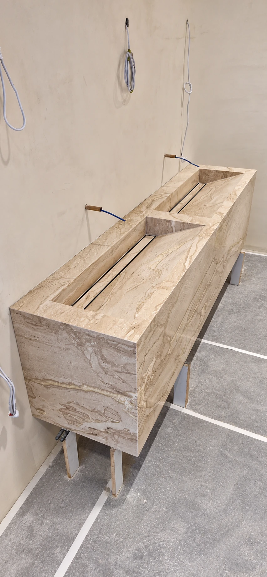 Custom beige veined stone double basin with geometric troughs and linear drain slots during installation