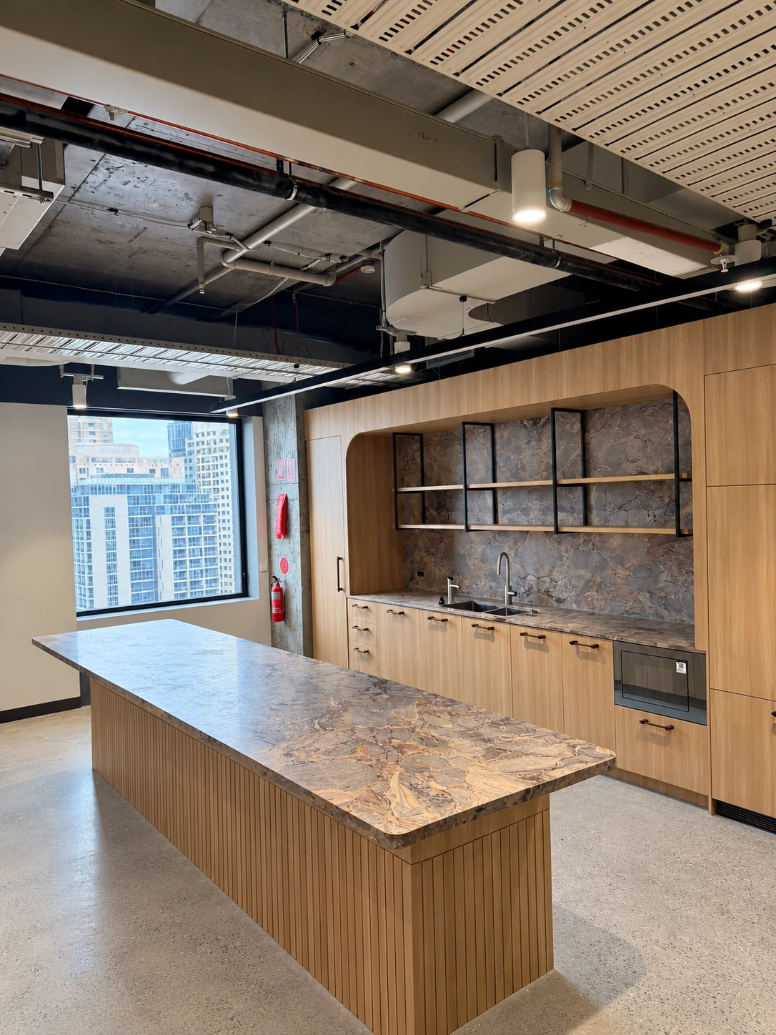 Office kitchen with veined stone island and matching splashback framed in timber