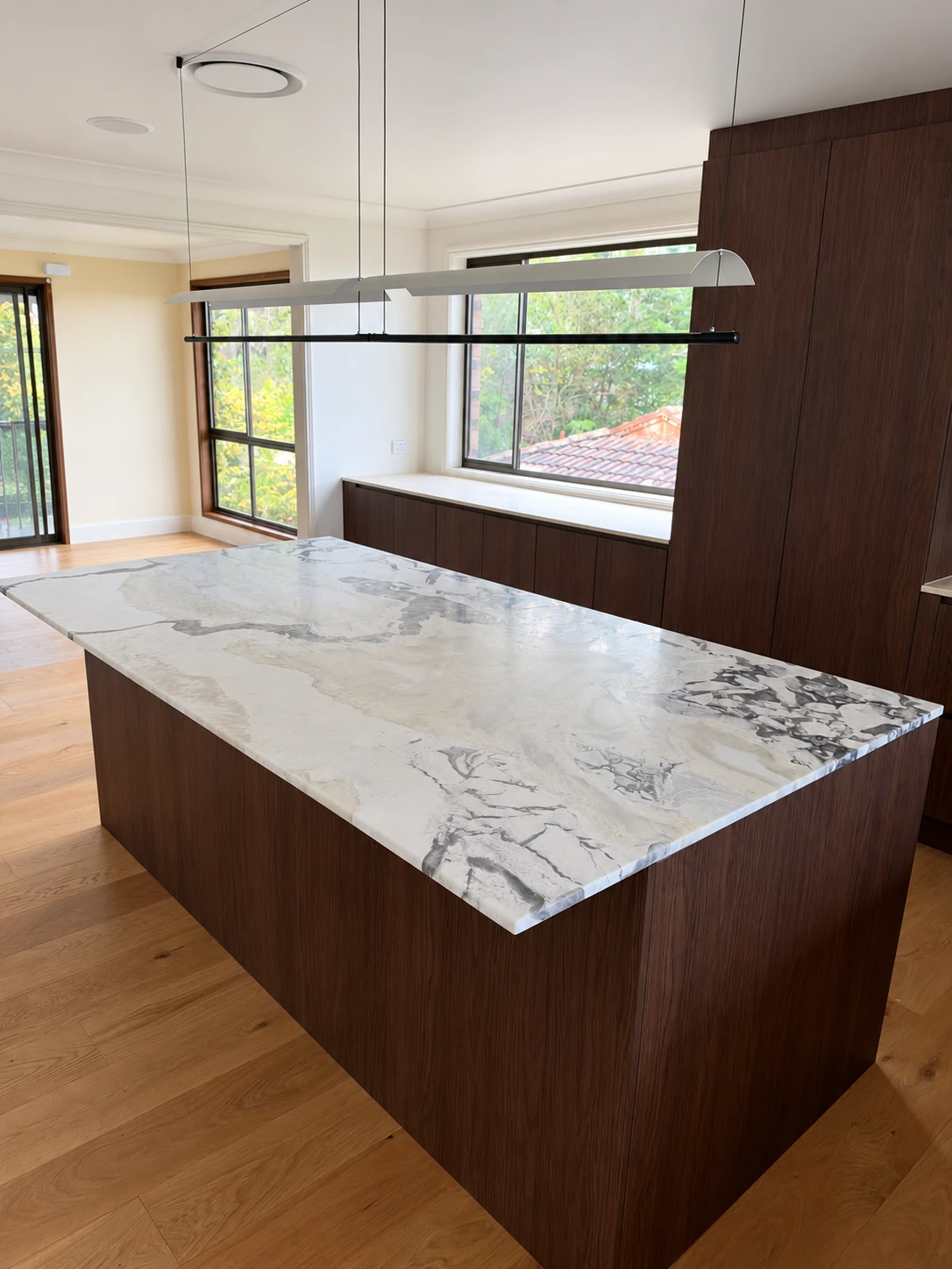White and grey veined natural stone island with dark timber cabinetry